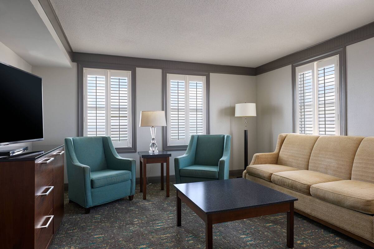 A hotel room with a TV, two armchairs, a sofa, a coffee table, and two lamps.