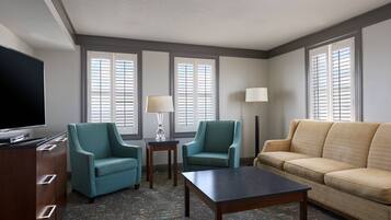 A hotel room with a TV, two armchairs, a sofa, a coffee table, and two lamps.