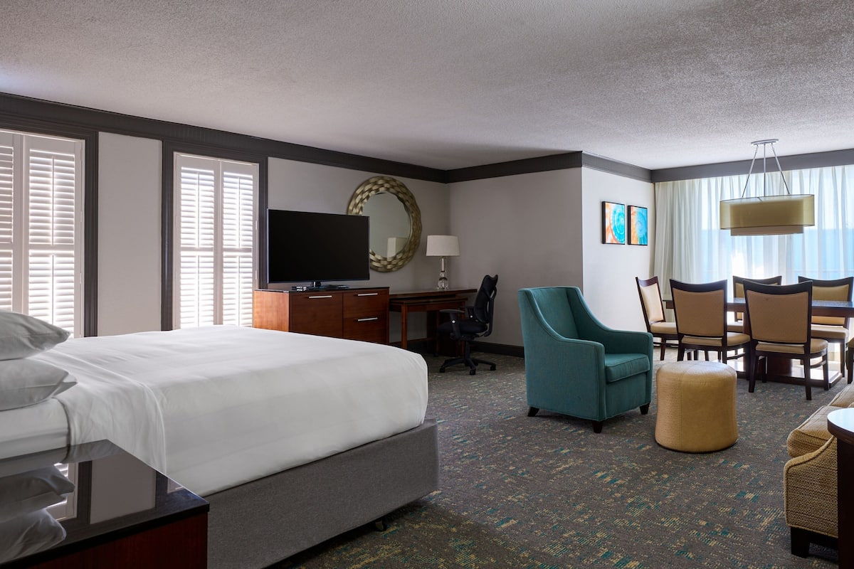 A hotel room with a bed, desk, chair, TV, and a dining area with chairs and a table.