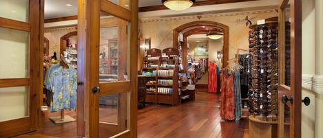Vestíbulo de un hotel boutique con pisos de madera, una escalera central y exhibición de ropa y accesorios.