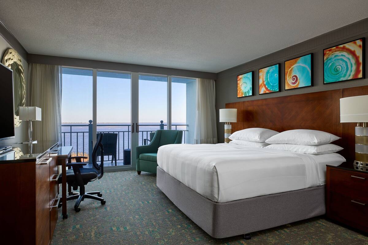 A hotel room with a large bed, a desk, a chair, and a view of the ocean.
