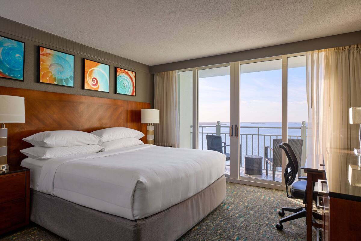 A hotel room with a large bed, a desk, and a view of the sea.