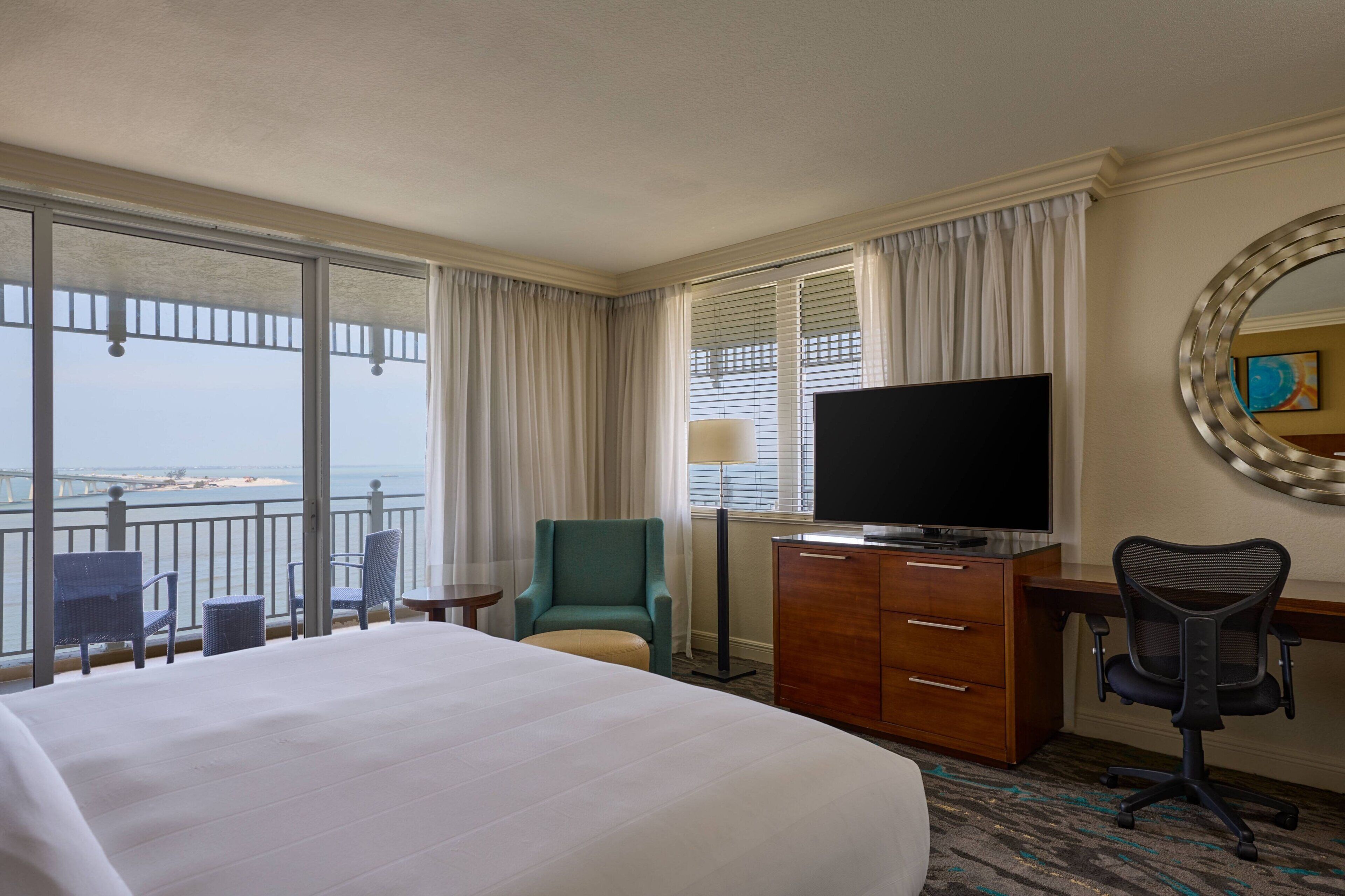 Ein Hotelzimmer mit einem großen Bett, einem Schreibtisch mit Computer, einem Fernseher und Blick aufs Meer.