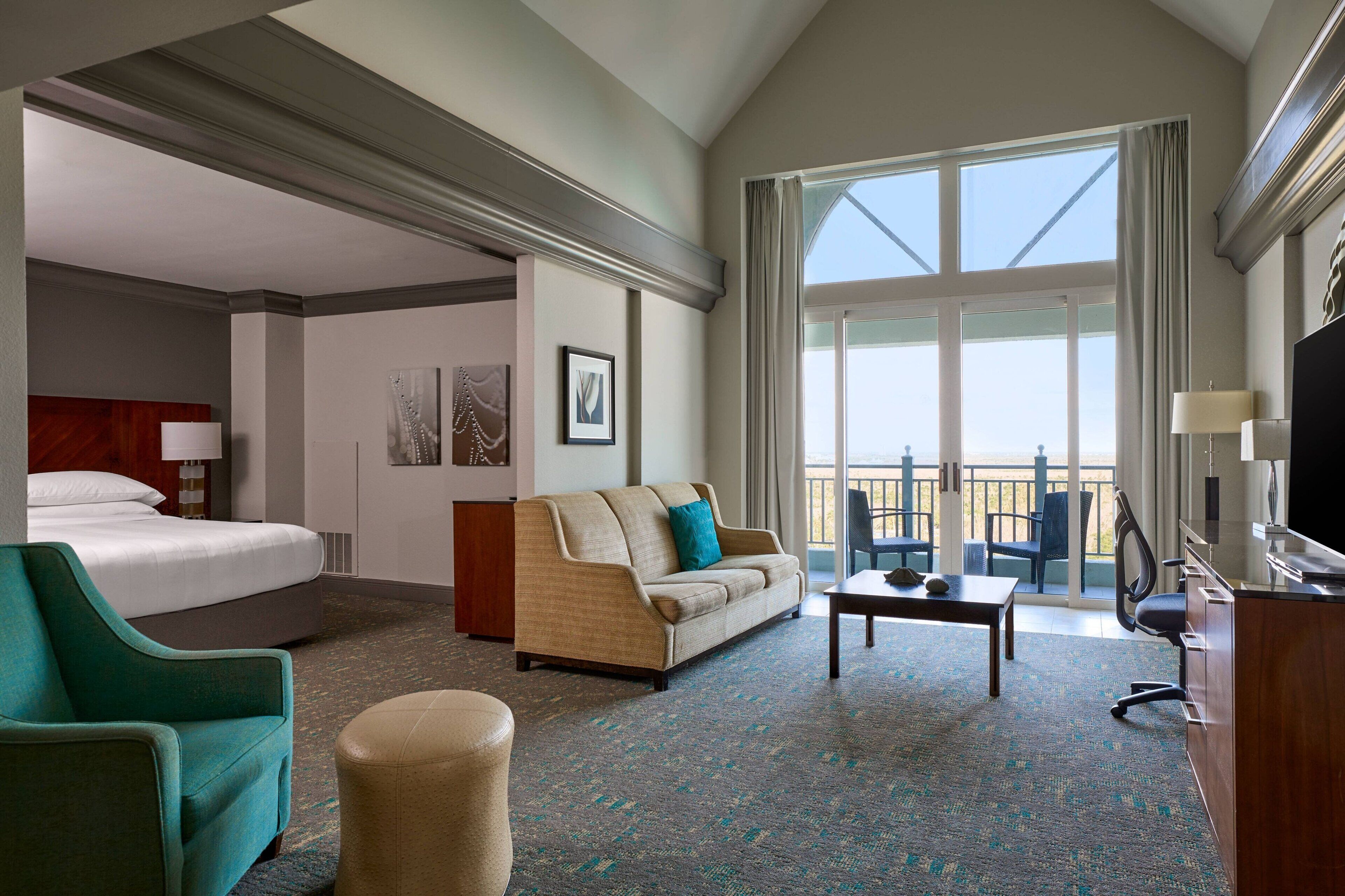 Habitación de hotel con cama, sofá, escritorio y balcón con vistas.