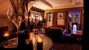 A dimly lit room with a bar area, a sofa, and a table set with wine glasses and a bottle. - The Vermont Hotel Newcastle (Newcastle-upon-Tyne)
