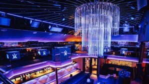 A modern bar area with a unique chandelier, multiple seating areas, and a bar counter with illuminated signage. - The Vermont Hotel Newcastle (Newcastle-upon-Tyne)