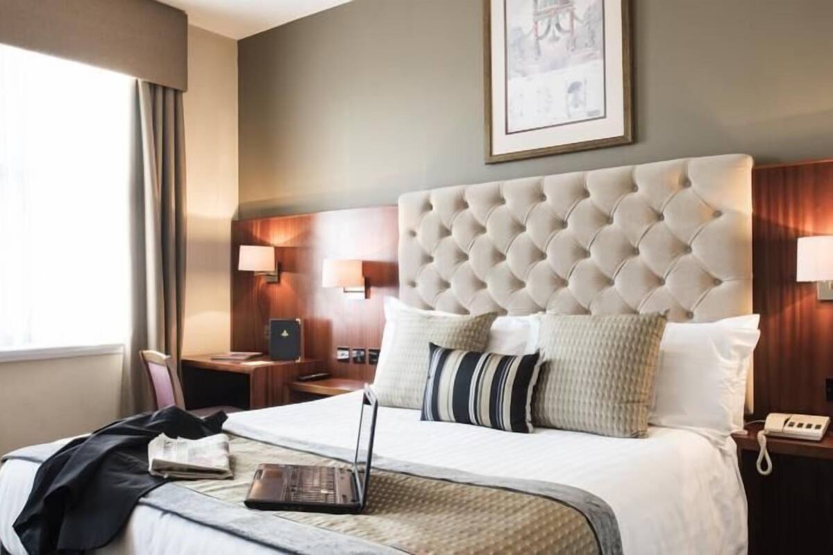 Une chambre d’hôtel avec un grand lit, un bureau, une chaise, un ordinateur portable et un téléphone.