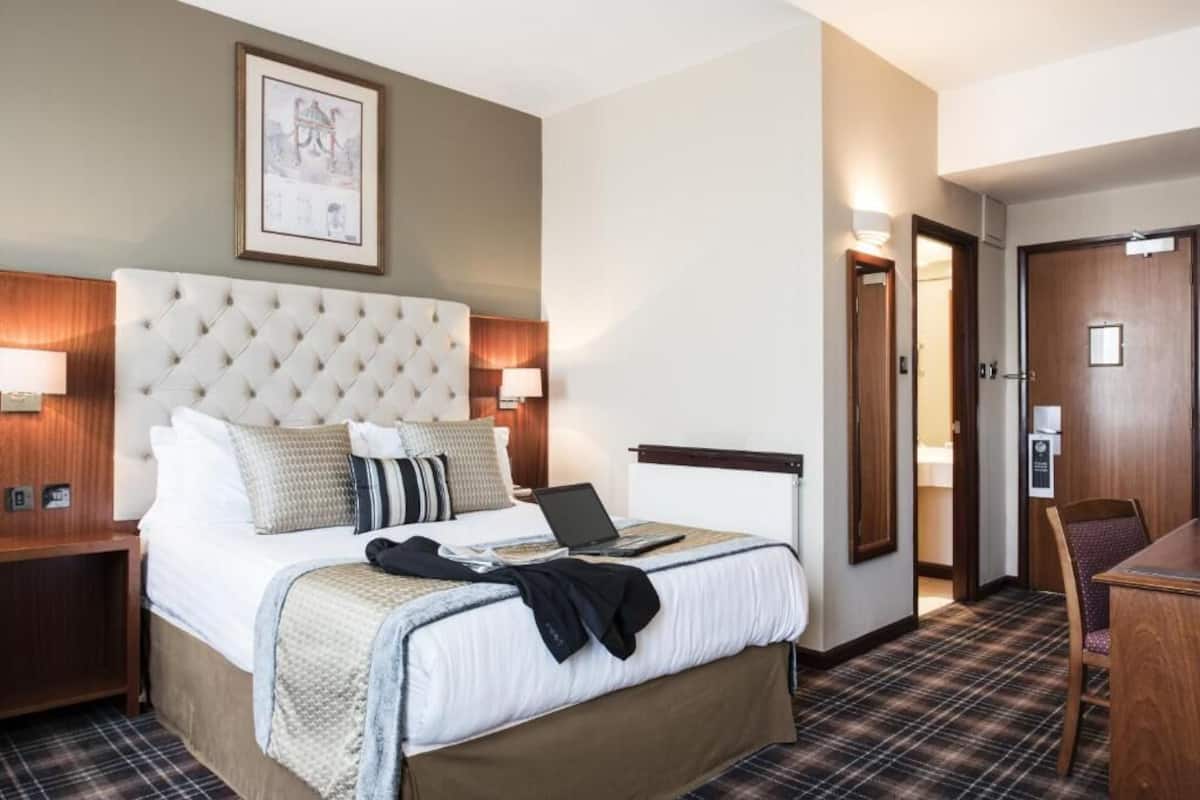 A hotel room with a tufted headboard, a bed with pillows, a laptop, a desk, and a chair.