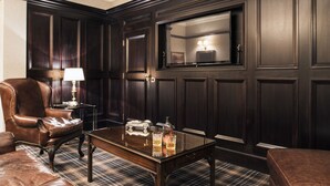 A dark wood-paneled room with a leather armchair, a small table with a lamp, and a glass cabinet. - The Vermont Hotel Newcastle (Newcastle-upon-Tyne)
