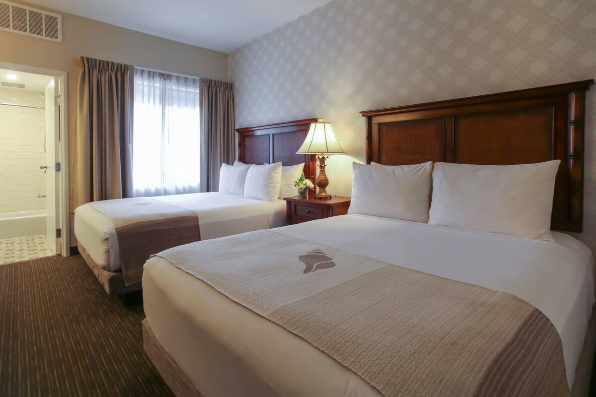 Een hotelkamer met twee bedden, een nachtkastje met een lamp, een badkamers deur en een behang met een patroon.