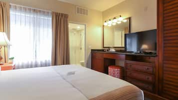 A hotel room with a large bed, a bathroom with a shower, a vanity with a mirror, and a television.