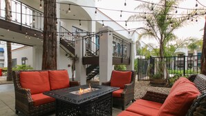 Un espacio de estar al aire libre con mobiliario de mimbre y cojines rojos, una chimenea y una escalera que conduce a un nivel superior.