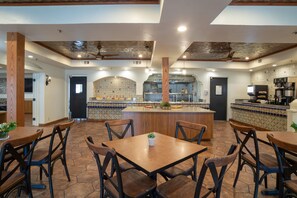 A restaurant with a central island, wooden chairs, and a tiled backsplash in the kitchen area.
