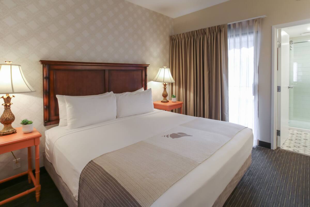 Een hotelkamer met een groot bed, twee nachtkastjes met lampen, een raam met gordijnen en een deur naar een badkamer.