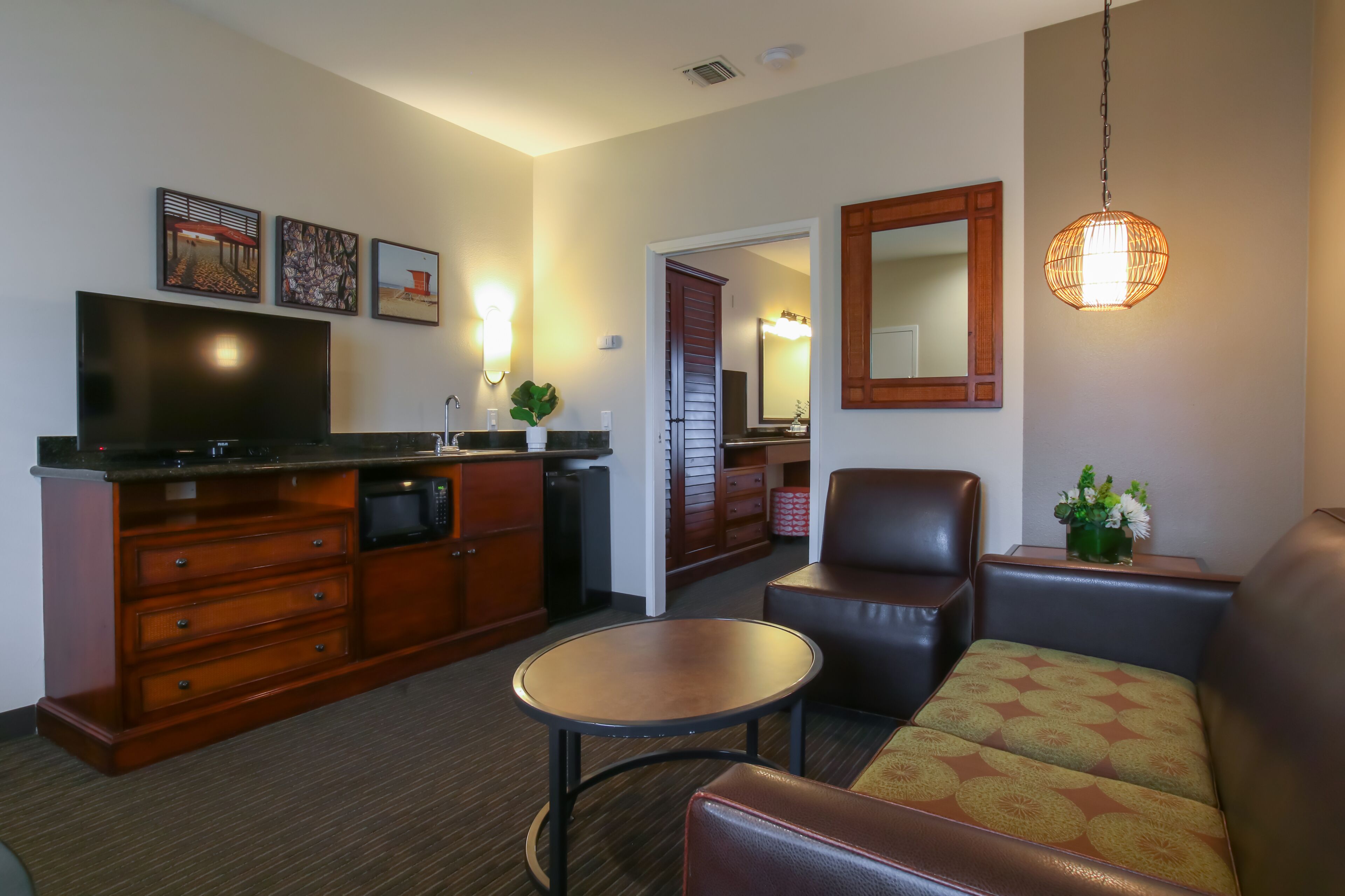 Un espacio habitable compacto con kitchenette, televisor de pantalla plana, mesa de comedor, sofá y lámpara colgante.