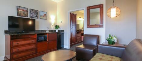 A living room with a sofa, a coffee table, a TV, a kitchen area with a microwave, and a dining table.