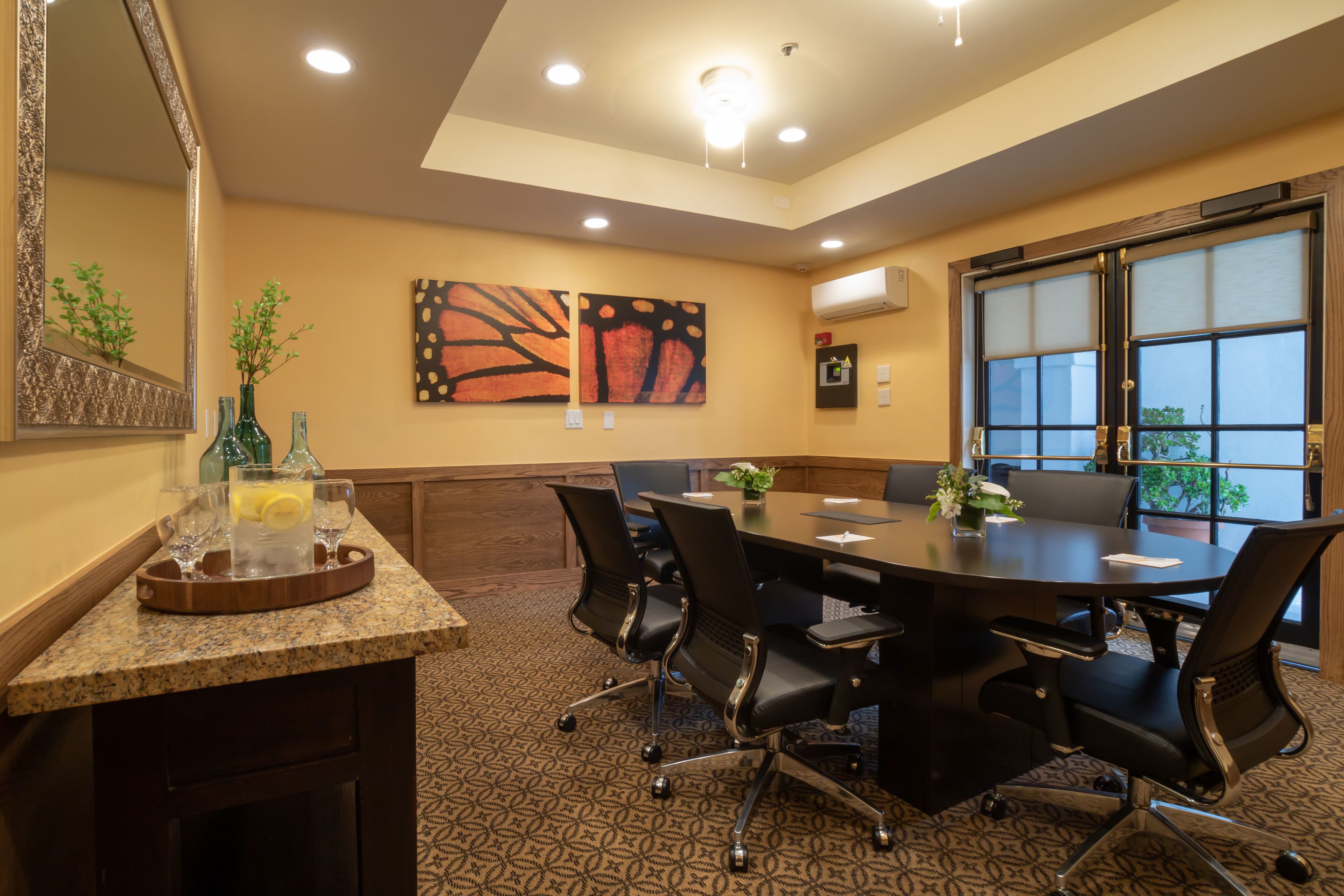 A conference room with a large table, black chairs, a wooden sideboard with glassware, and artwork on the walls.