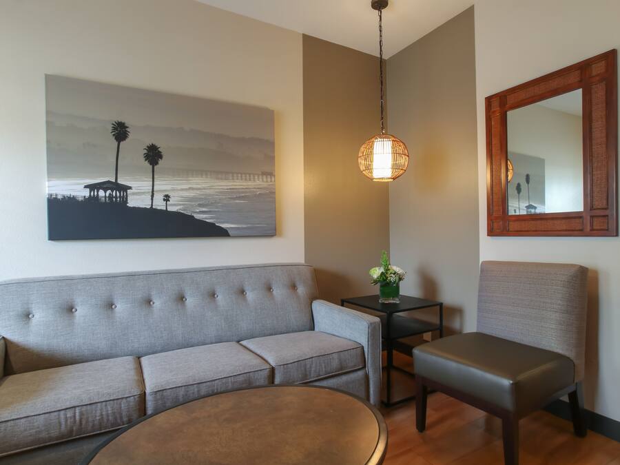 Un salon moderne avec un canapé gris, une table basse ronde, une petite table d’appoint sur laquelle est posé un vase, et un grand miroir accroché au mur.