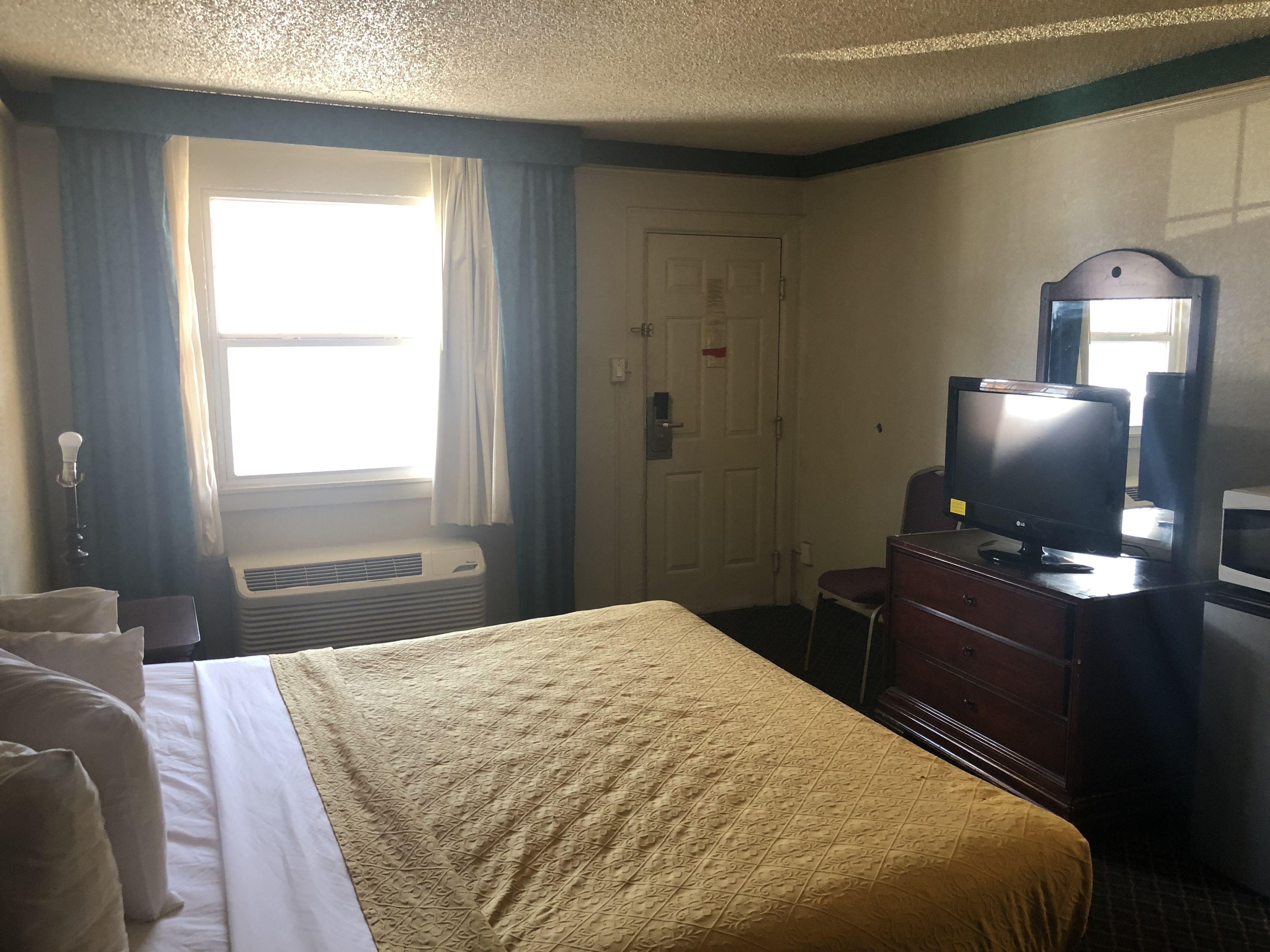Habitación de hotel con cama, televisor, cómoda y ventana con cortinas.