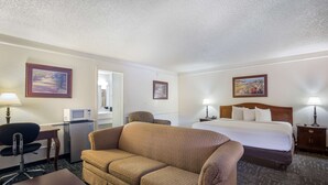 A hotel room with a bed, a sofa, a desk with a computer, a microwave, and a lamp.