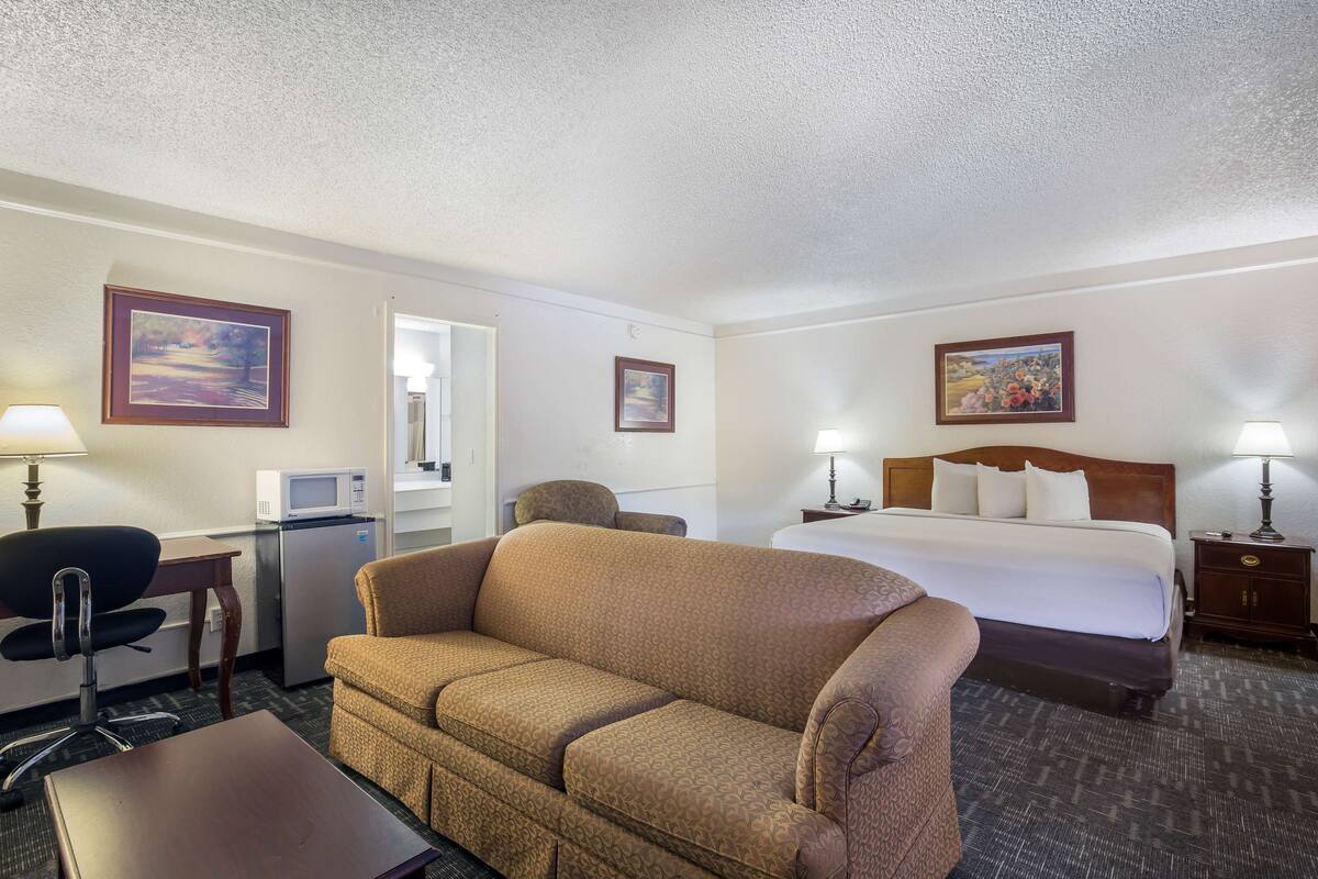 A hotel room with a bed, a sofa, a desk with a computer, a microwave, and a lamp.