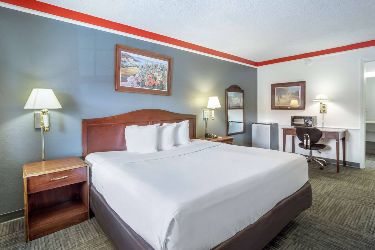 A hotel room with a large bed, two bedside tables with lamps, a desk with a chair, and two wall-mounted lamps.