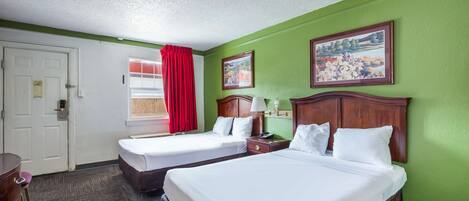 Habitación de hotel con dos camas, cabecera de madera, mesita de noche con lámpara, escritorio con silla y ventana con cortinas rojas.