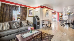A hotel lobby with a sofa, a coffee machine, and a dining area with chairs and tables.