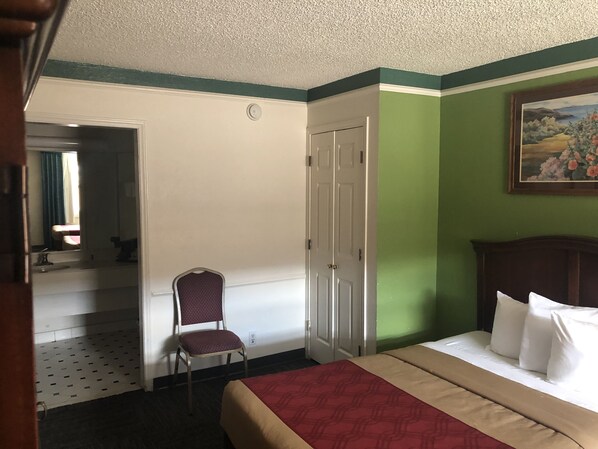 A hotel room with a bed, a chair, a door, and a painting on the wall.