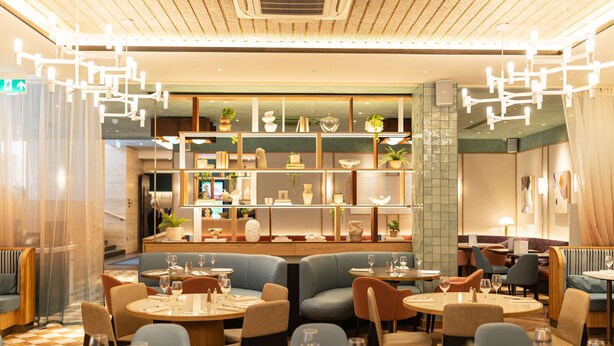 Ein Restaurant mit runden Tischen und Sitzecken, ein Barbereich mit Regalen voller Dekoration und eine moderne Chandelier.
