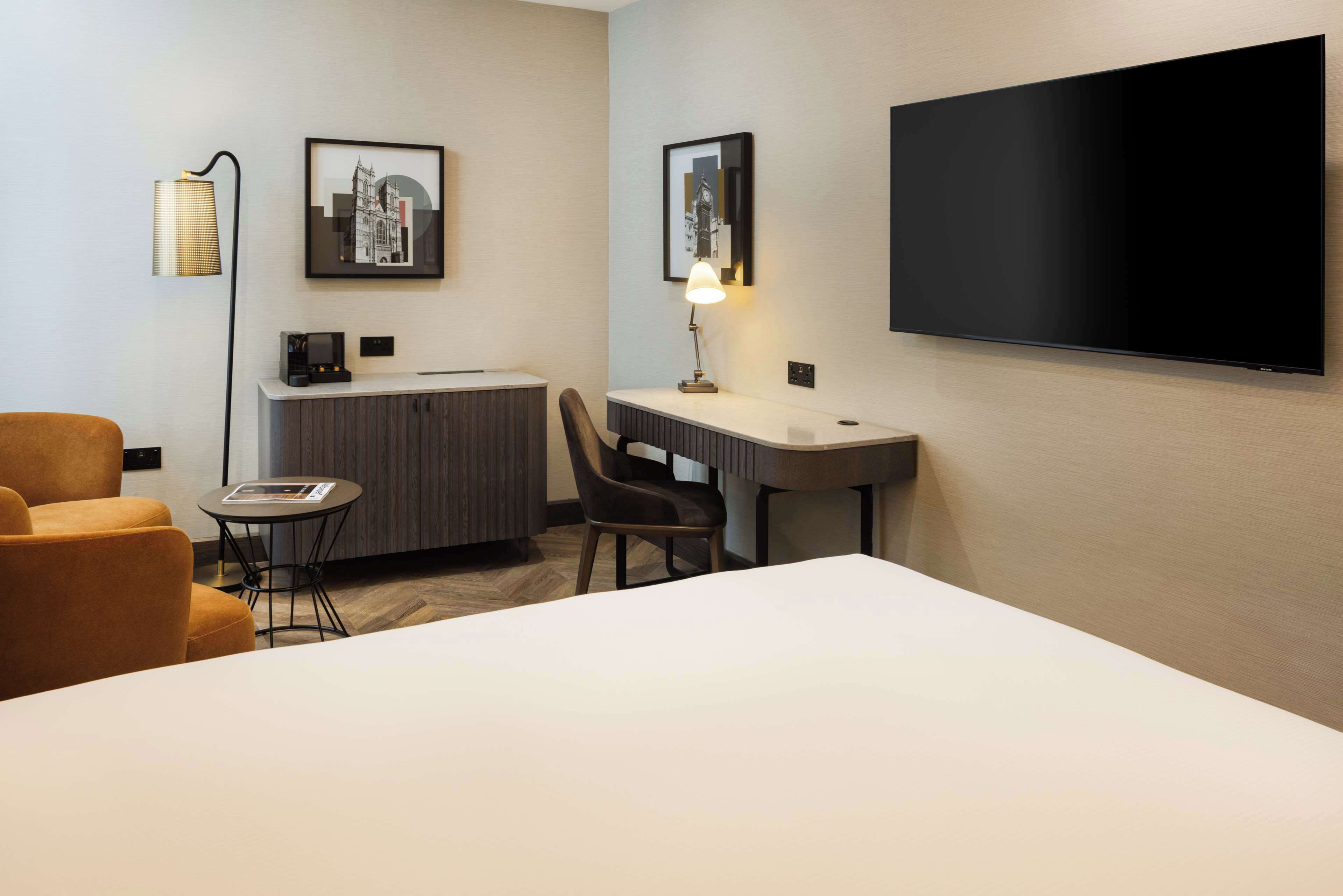 A hotel room with a bed, a desk, a chair, a sofa, a TV, and a lamp.