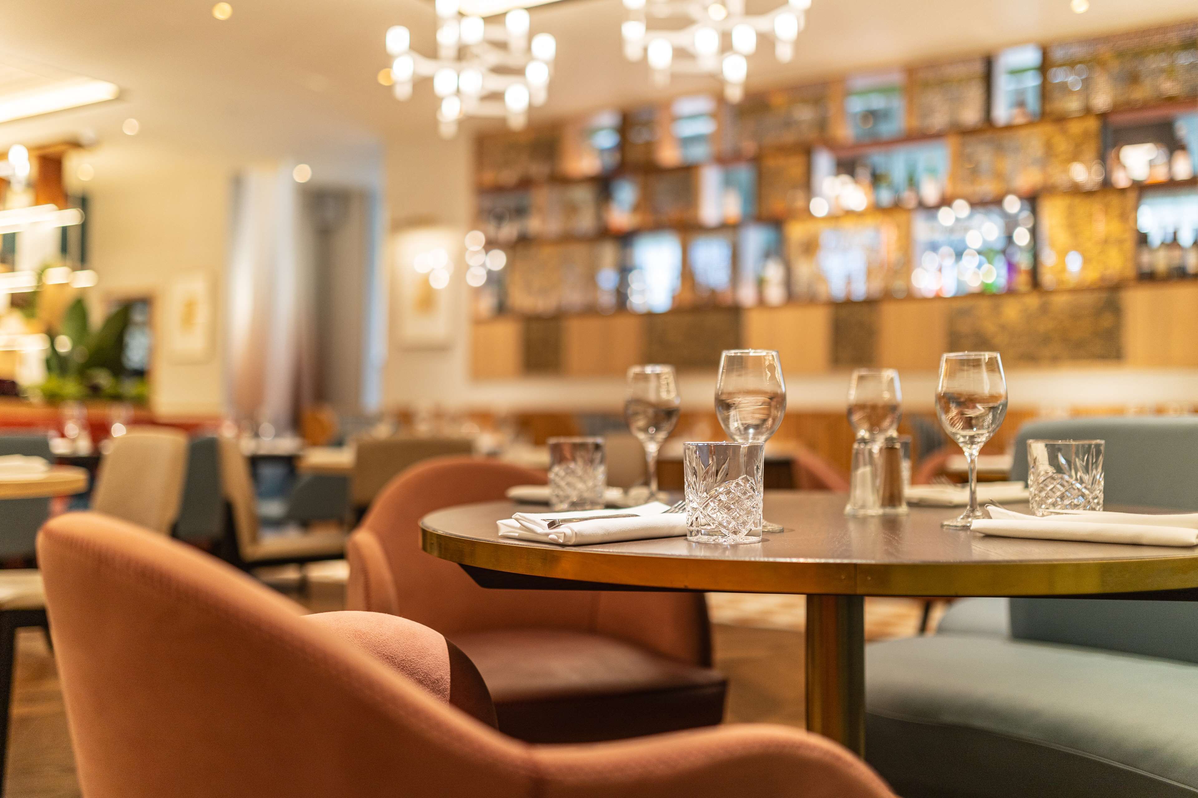A restaurant interior with round tables, cushioned chairs, and a bar area with shelves of bottles.