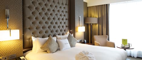Hotellihuone, jossa on suuri sänky, koristeltu pääty, yöpöytä lampun kanssa, tuoli ja pieni pöytä, jonka päällä on kuppi ja kirja.