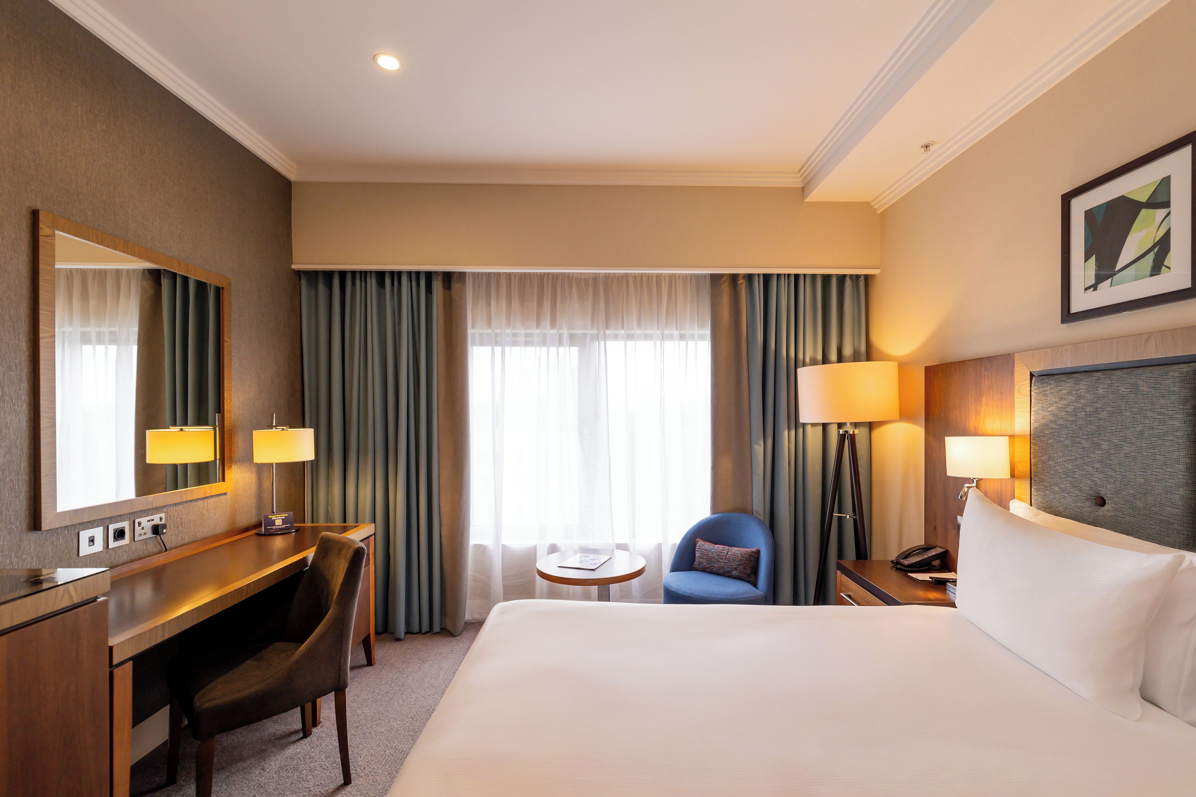 Een hotelkamer met een groot bed, een bureau met stoel, een bijzettafeltje, een lamp en een grote spiegel.