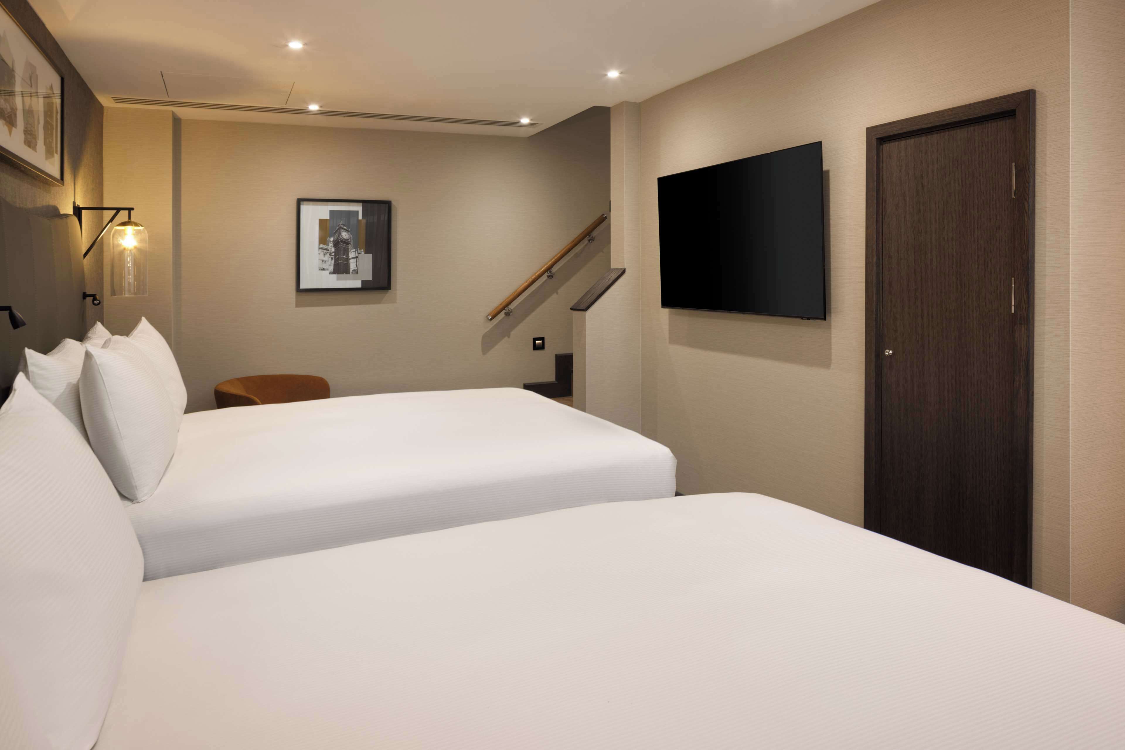 Une chambre d’hôtel avec deux lits, un téléviseur fixé au mur, une chaise en bois et une porte.