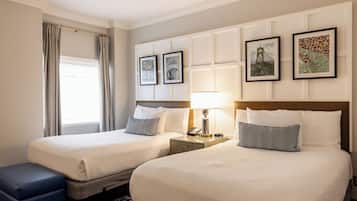 Quarto de hotel com duas camas, uma mesa de cabeceira com abajur, telefone e quadros na parede.