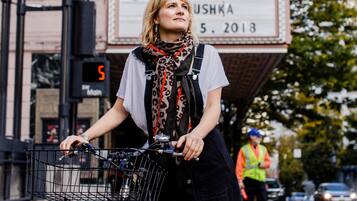 Una persona dempeus al costat d'una bicicleta amb cistella, davant d'un cartell de teatre que anuncia una actuació.