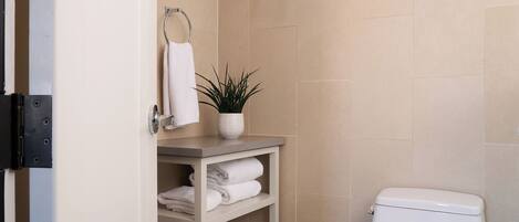Un baño moderno con inodoro, un estante con toallas y una planta en maceta.