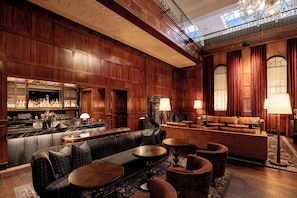 Un vestíbulo amplio con área de bar, diferentes disposiciones de asientos y un alto techo con paneles de madera ornamentados.