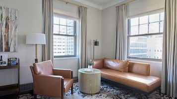 Een moderne hotelkamer met een leren bank, een ronde salontafel en een groot raam met uitzicht op de stad.