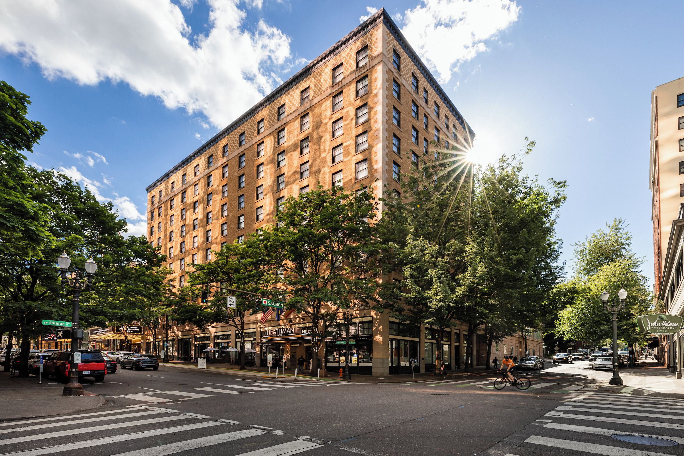 A multi-story building with a brick facade, located at a street corner with crosswalks and trees.