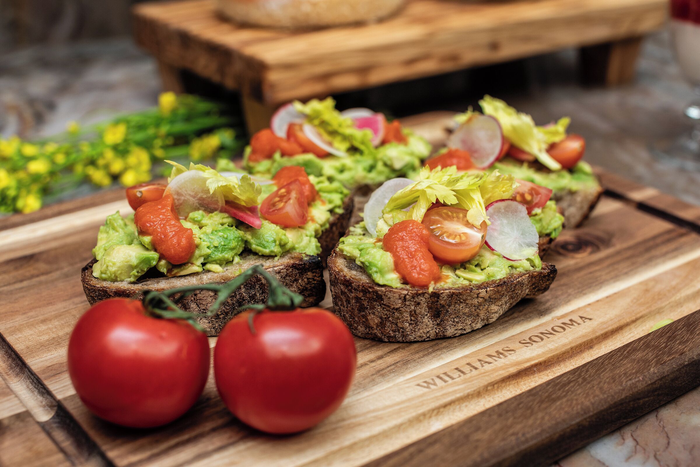 Cuatro sándwiches abiertos con aguacate, tomate y lechuga sobre una tabla de madera.