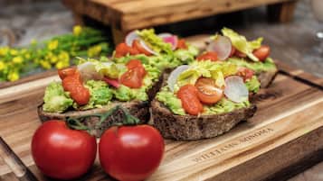 Cuatro sándwiches abiertos con aguacate, tomate y lechuga sobre una tabla de madera.