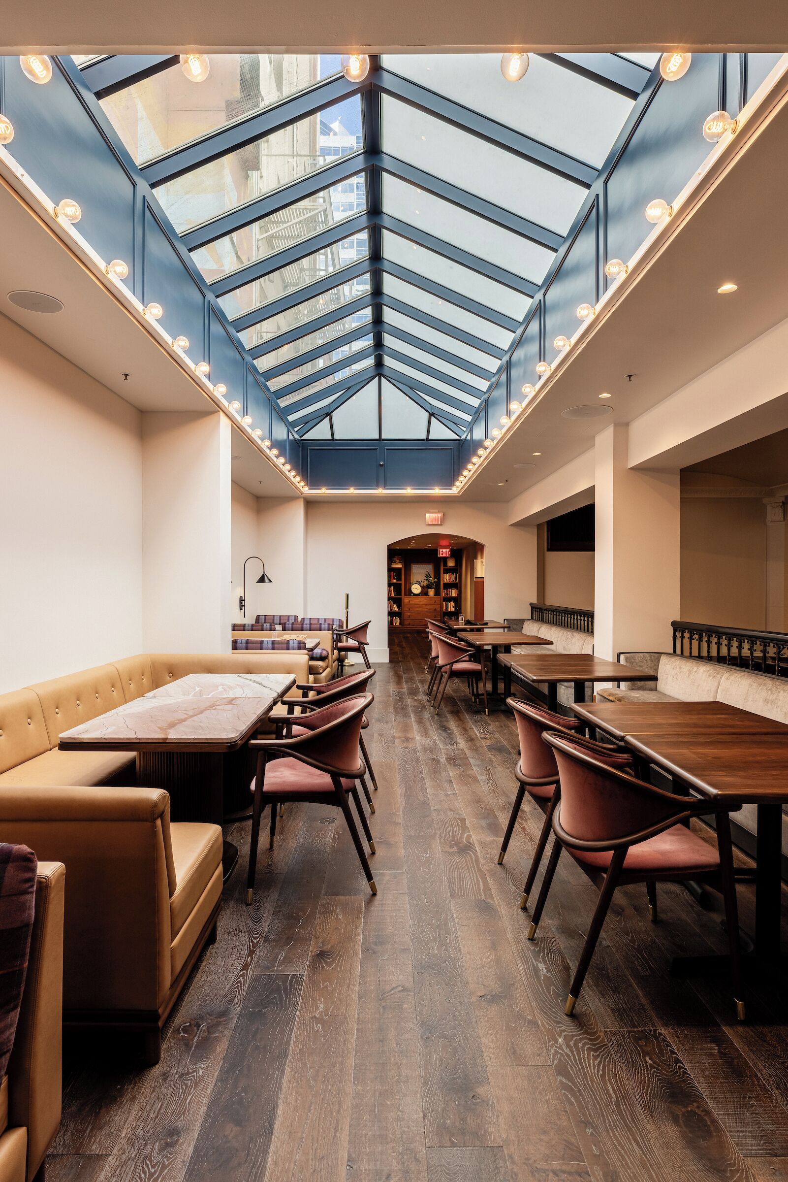 Ein großzügiges Restaurant mit hoher Decke und Oberlichter, Holztische und -stühle sowie eine zentrale Sitzgruppe mit einer Bank.