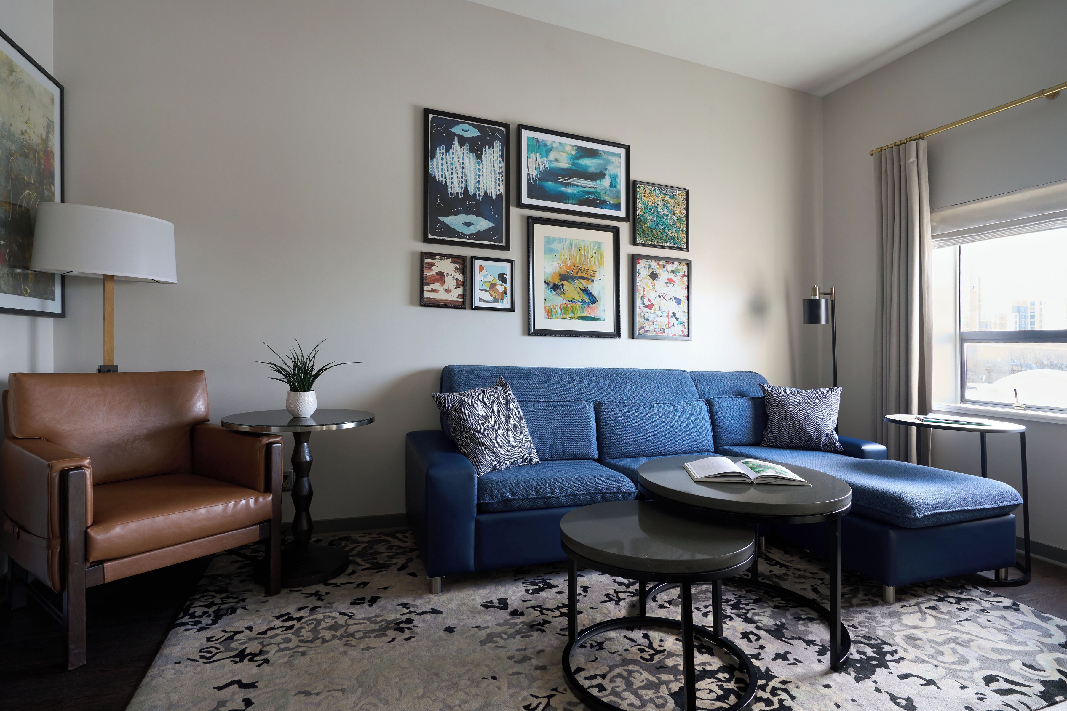 A modern living room with a blue sofa, a brown leather chair, a small round table, and a floor rug.