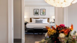 A hotel room with a bed, bedside tables, a nightstand, a lamp, a vase with flowers, and a framed picture on the wall. - Heathman Hotel (Portland)