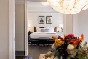 Una habitación de hotel con cama, mesitas de noche, lámpara, un jarrón con flores e imagen enmarcadas en la pared.