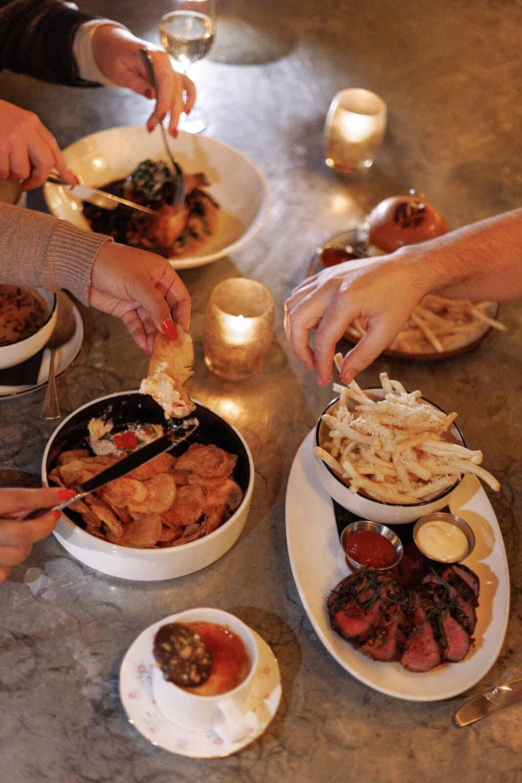 Una mesa de comedor con varios platos, incluyendo papas fritas, un tazón de chips y un bistec con acompañamientos.