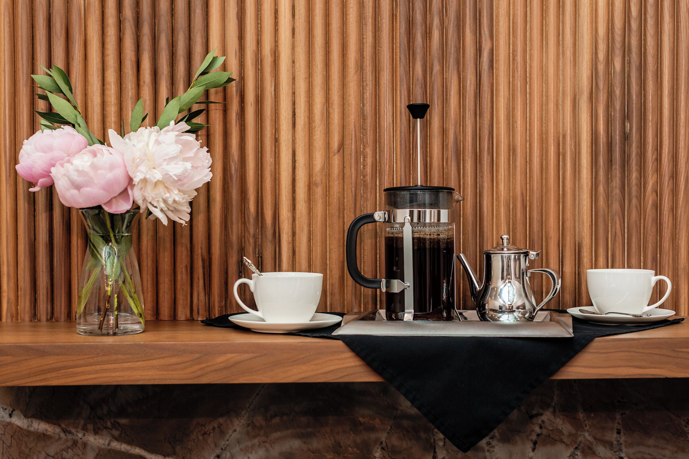 Un tavolo in legno con una macchina da caffè, due tazze bianche e un vaso con fiori.