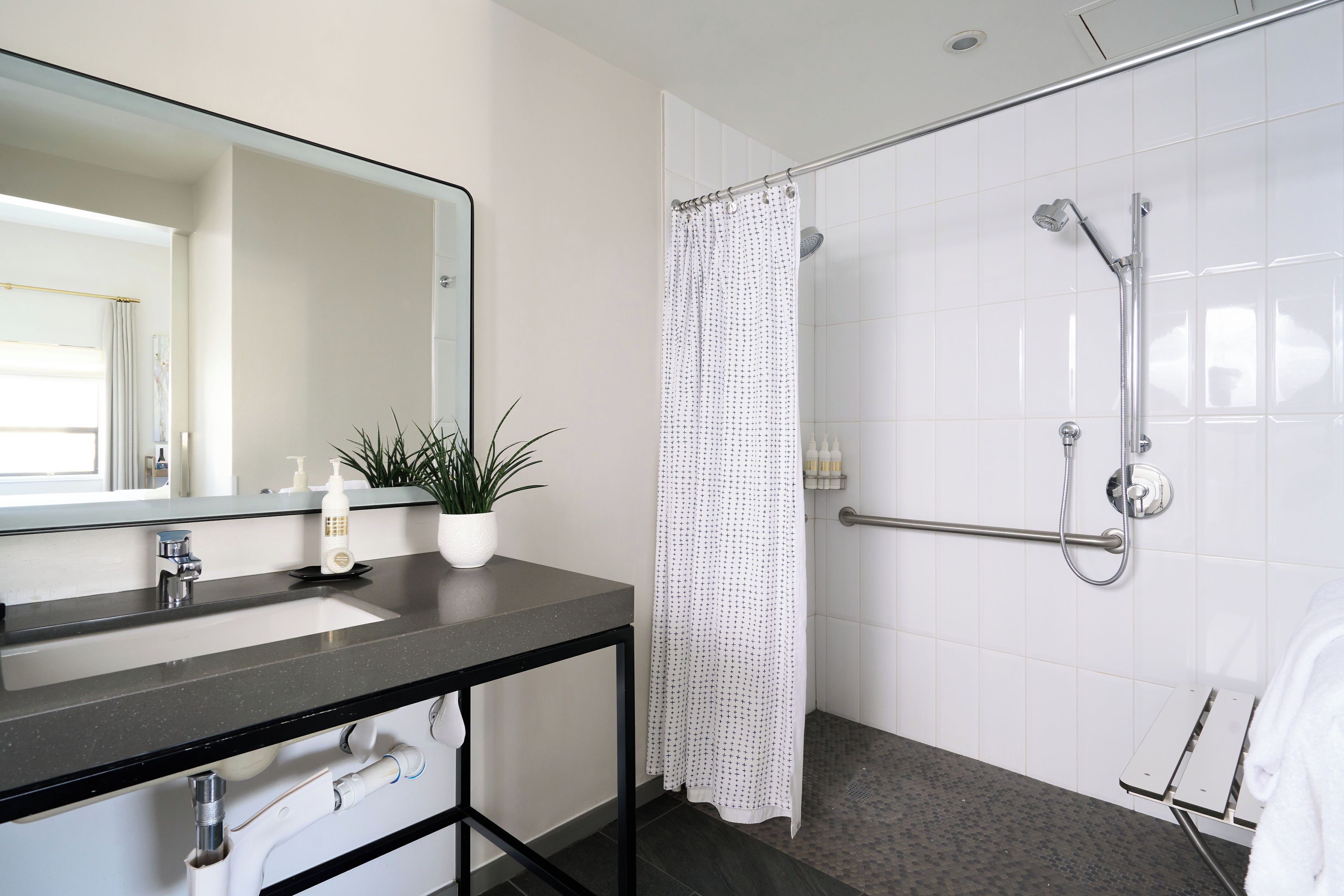 Un baño moderno con lavamanos de encimera negro, un espejo, una ducha con cabezal de ducha de mano y cortina de ducha blanca.